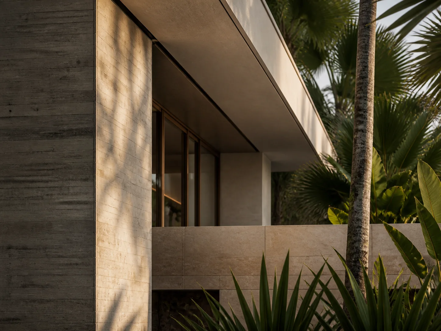 Close view of board-formed concrete, honed limestone, bronze-framed glass, and tropical foliage.